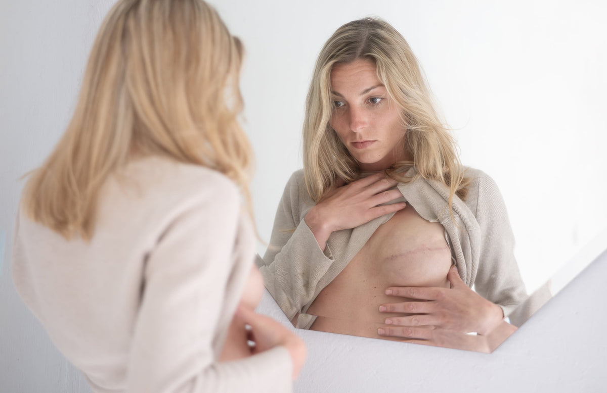 A woman looks at her mastectomy scar. Mastectomy scars follow their own healing timeline. Here's what to expect, the different scar types, and what actually supports the healing process.