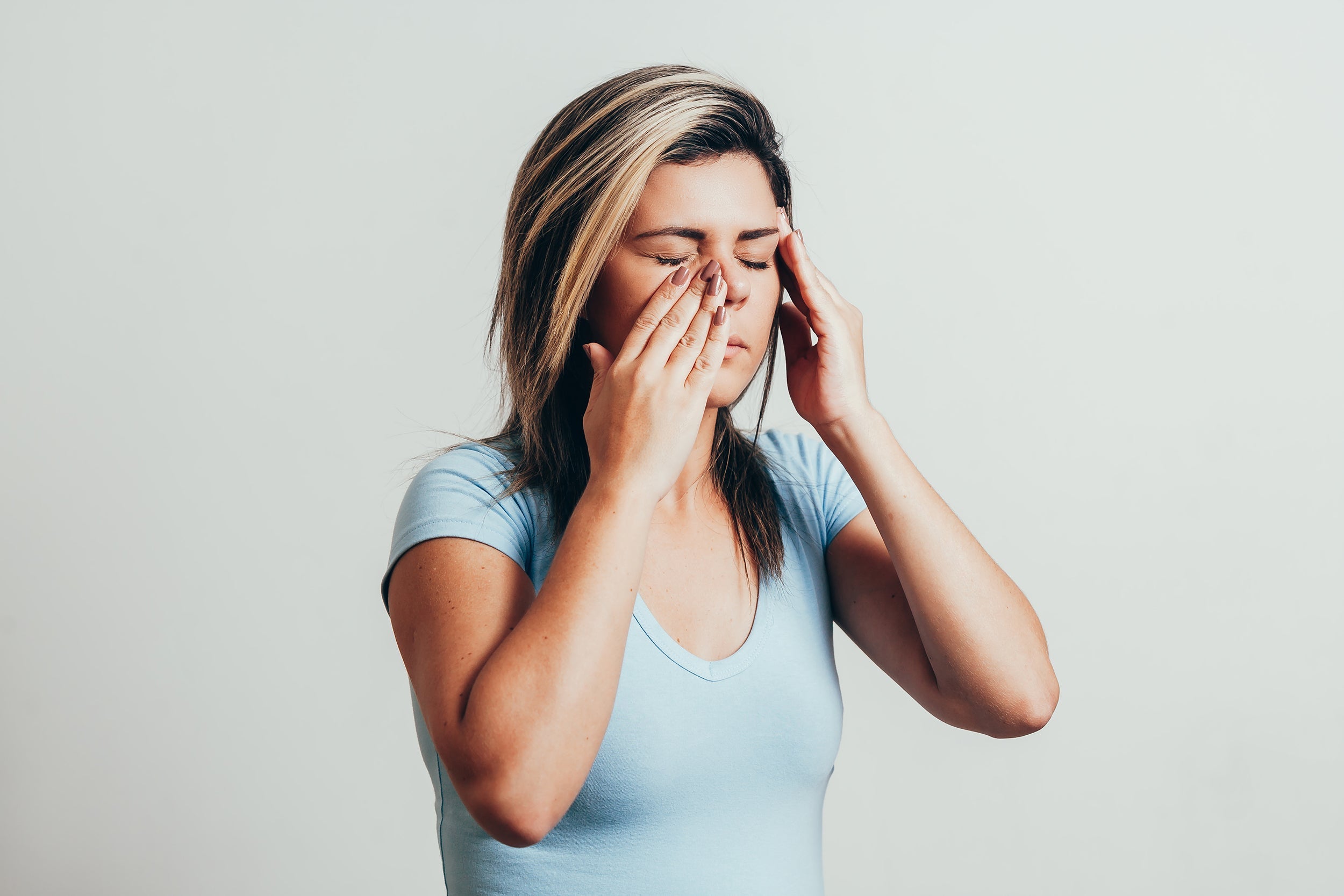 A woman holds her sinus area in discomfort. If you're preparing for sinus lift surgery, learn how to reduce swelling with our complete guide.