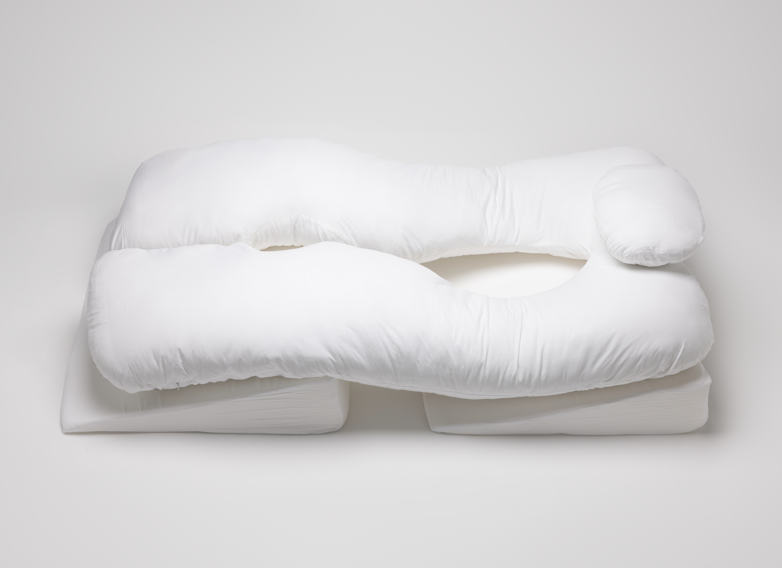 A large, white, U-shaped body pillow with side openings and an attached headrest, placed on a plain white surface.