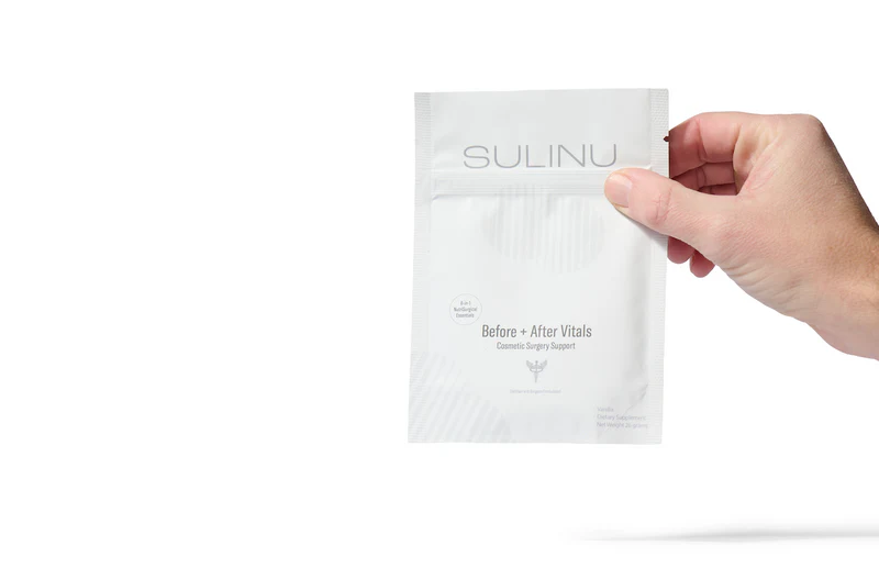 A hand holds a white packet labeled The VIP Surgical Recovery Kit, designed to aid cosmetic surgery recovery, against a plain white background.