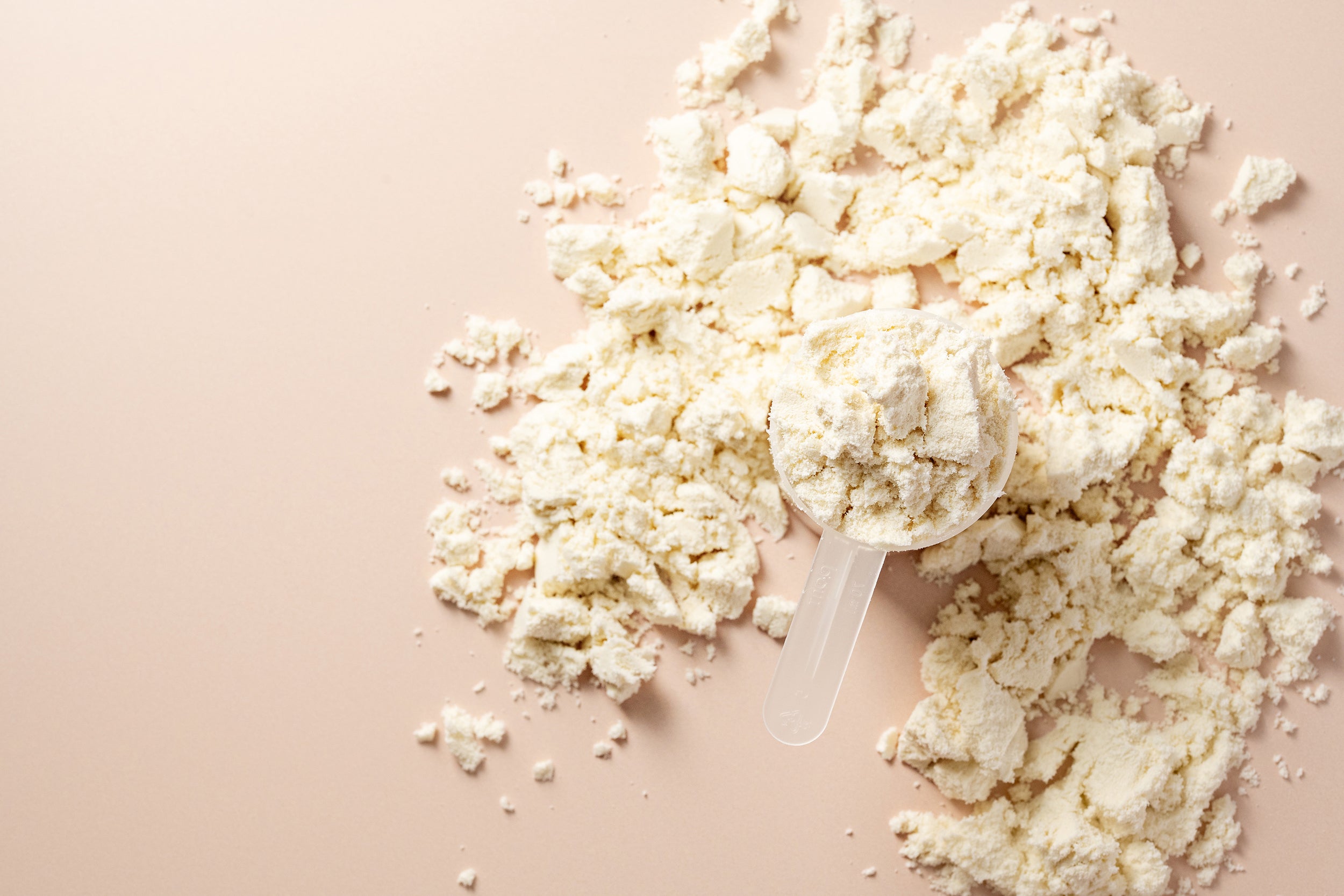 A plastic scoop filled with The Prep Starter Kit protein powder rests on a beige surface, surrounded by scattered powder—an uncomplicated yet essential part of healing nutrition recommended by a surgical dietitian.