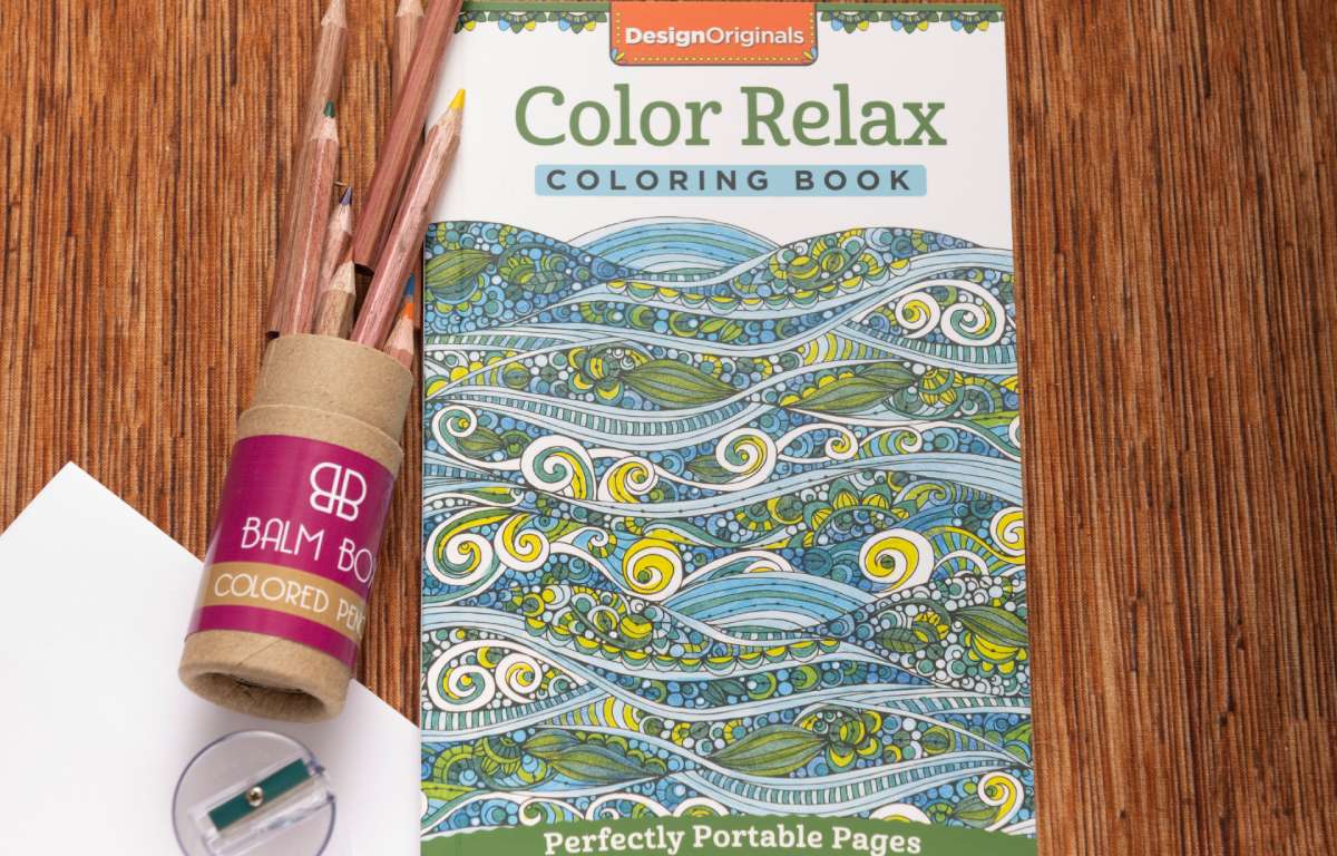 The Best Mastectomy Care Package, featuring a coloring book with a blue and green wave cover, colored pencils, and a sharpener, is shown on a wooden surface—an ideal gift for cancer patients.