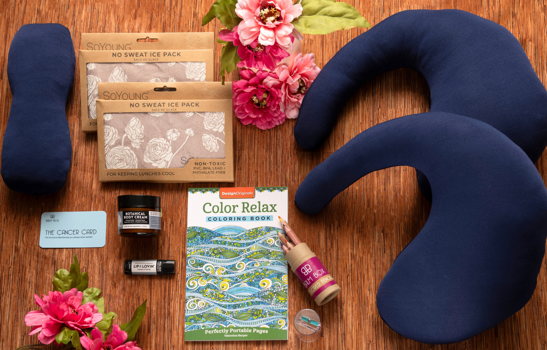 The Best Mastectomy Care Package features neck pillows, an eye mask, ice packs, a coloring book with colored pencils, lip balm, a candle, and pink artificial flowers—thoughtfully curated for relaxation and self-care after surgery.