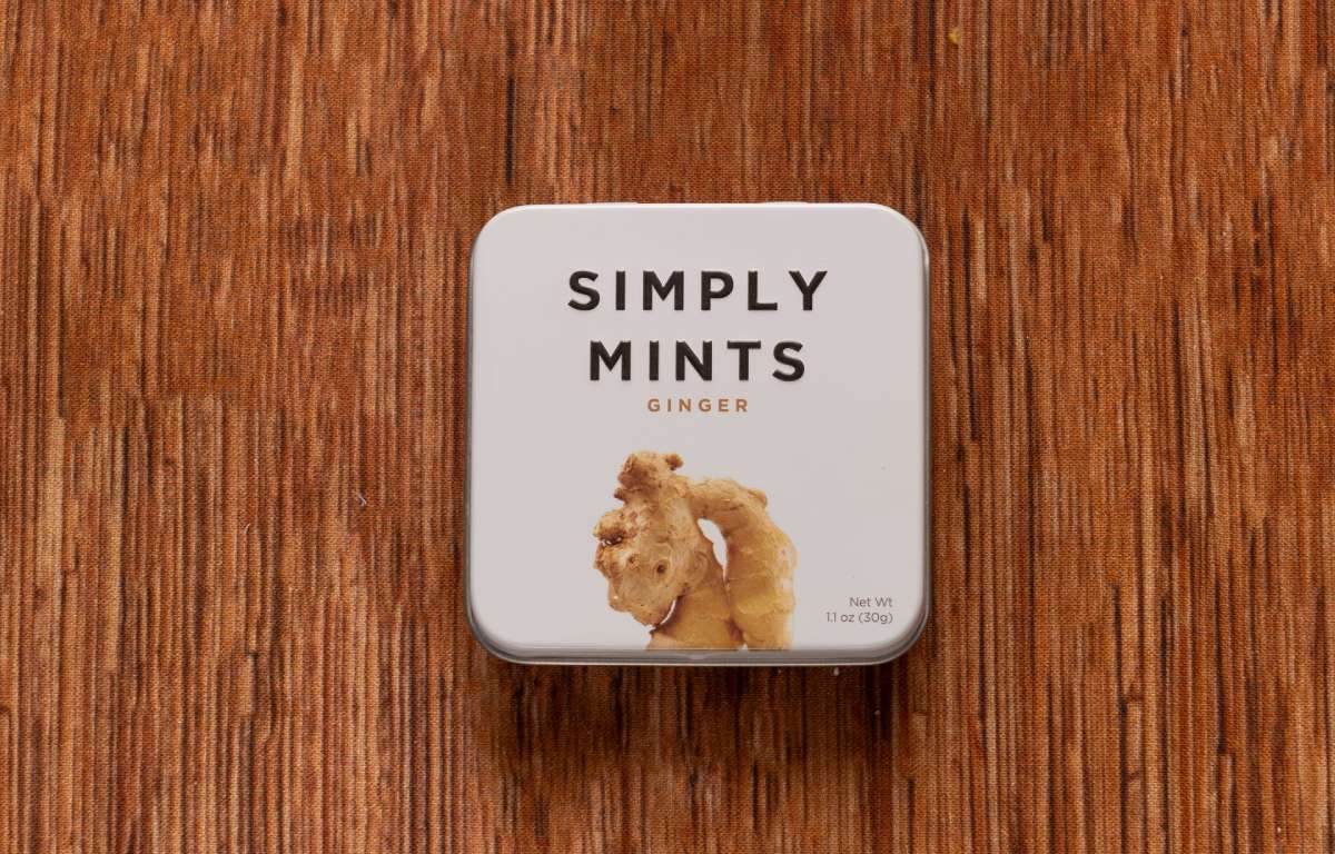 A square tin labeled "The Perfect Little Anti-Nausea Box" sits on a wooden surface. The white lid features an image of ginger and bold black text, making it ideal for nausea relief during chemotherapy side effects.