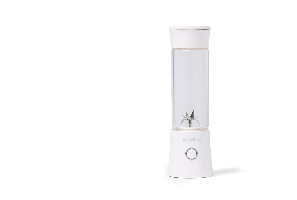 The Personal Blender features a white base with a clearly visible power button, a transparent container showcasing its metal blades inside, and is displayed on a plain white background.