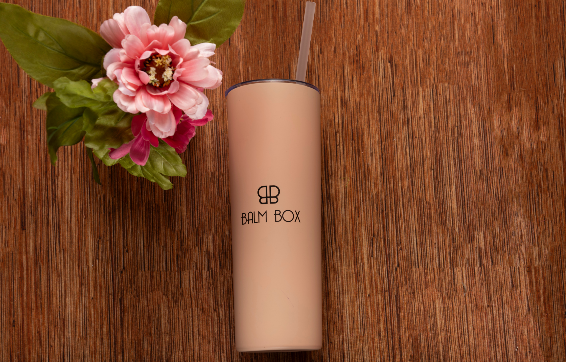 The Perfect Little Anti-Nausea Box features a beige tumbler with straw and BALM BOX logo, shown on a wooden surface beside a pink artificial flower—an ideal gift to help cancer patients manage chemotherapy side effects.
