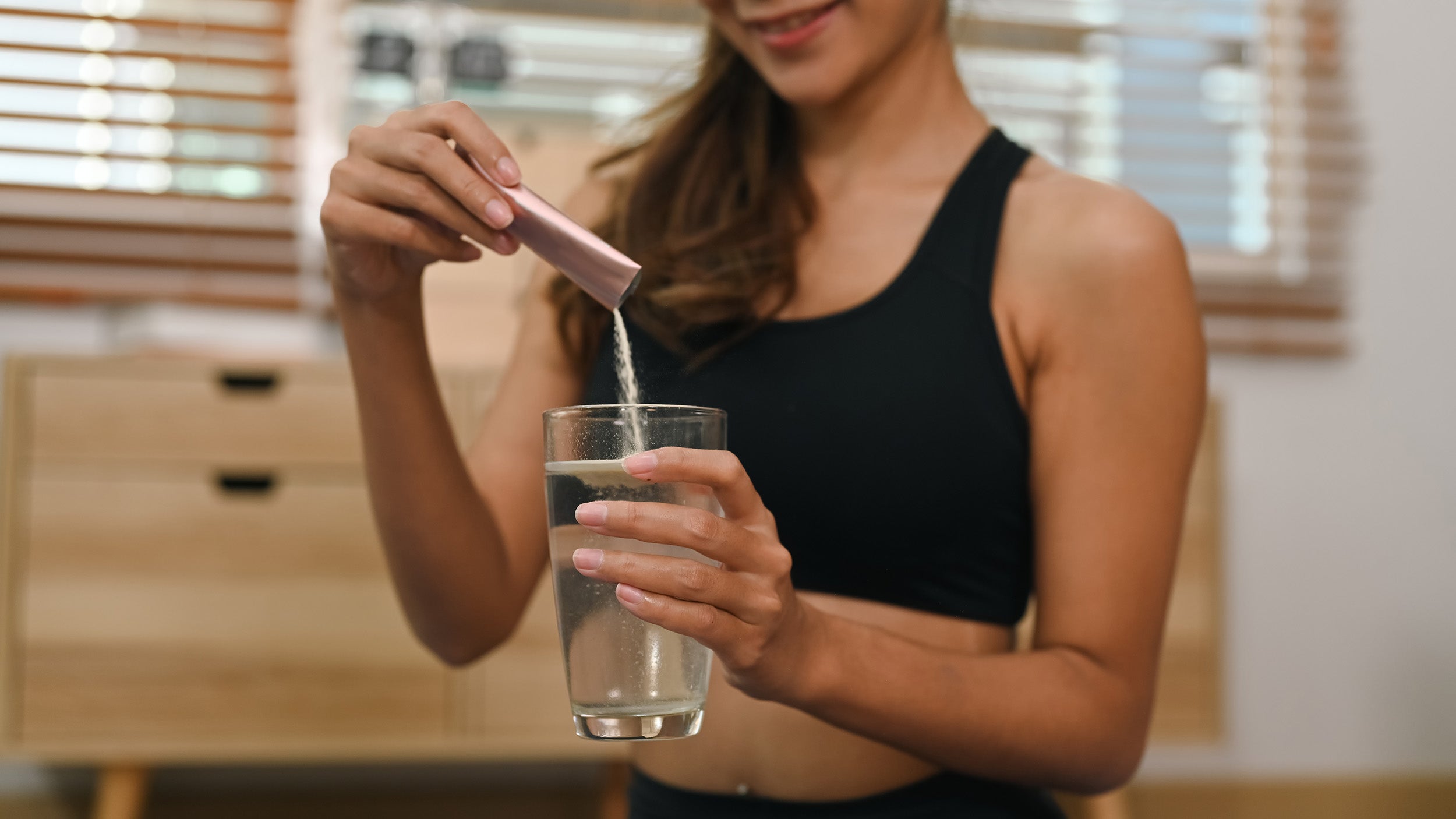 A woman pours a supplement into water. Does collagen help after surgery? Read more in our complete guide.