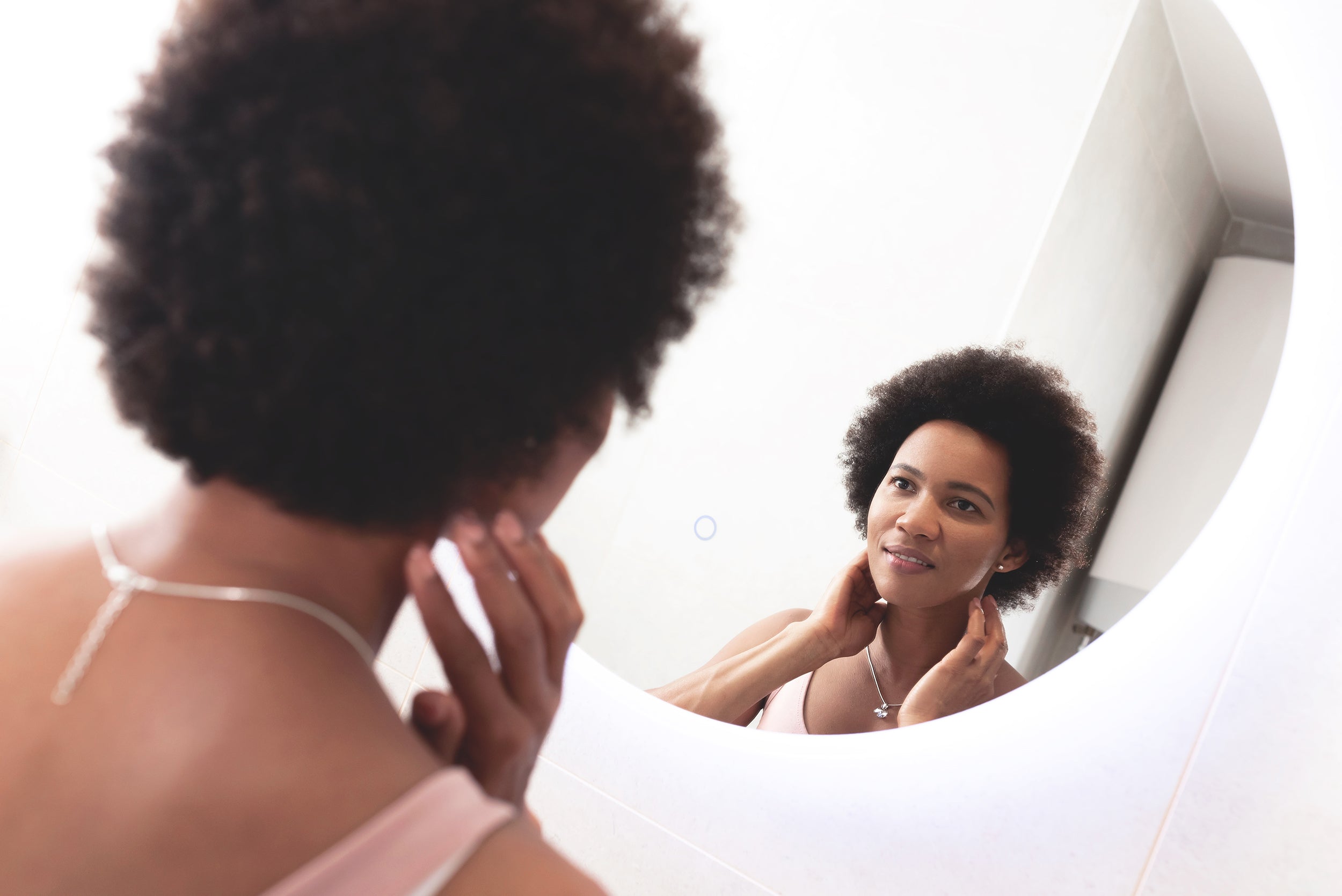 A woman looks at herself in the mirror. Understand everything you need to know about post facelift swelling in our complete guide.