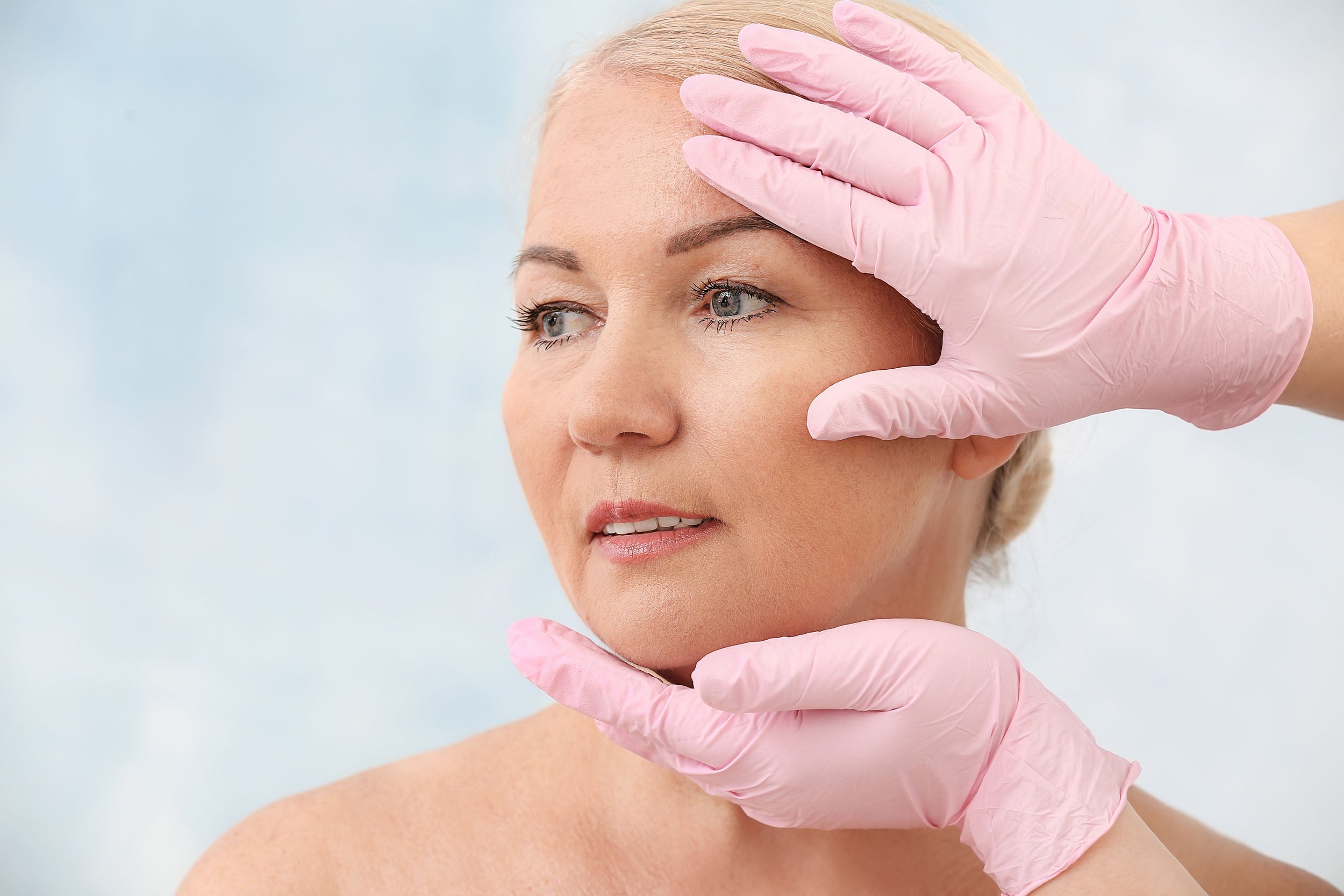 A physician examines a woman's face. If you're preparing for a fat transfer to the face, you might be wondering about swelling. Check out our complete guide on swelling after fat transfer to the face.