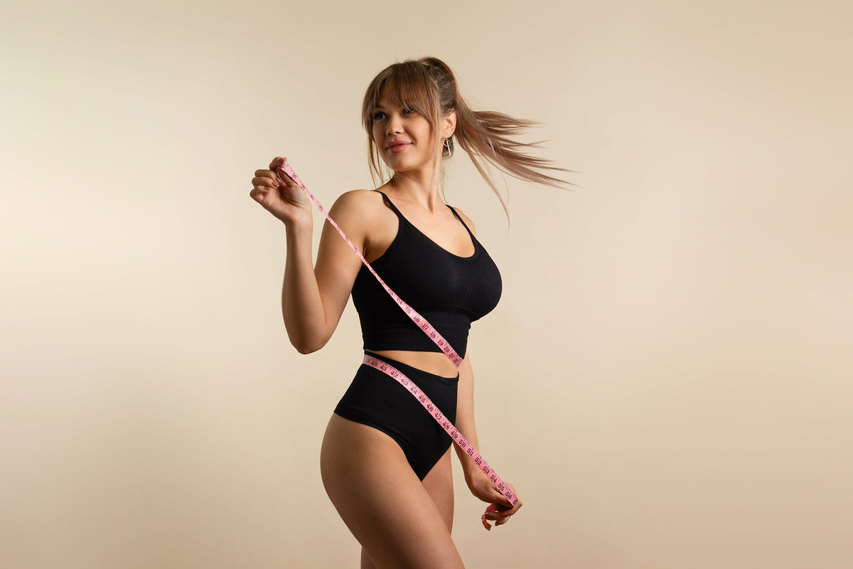 A woman in her underwear measures her stomach. If you've been wondering what to eat before and after a tummy tuck, check out our complete guide to support your healing journey.